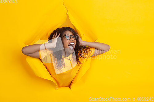 Image of Cheerful young woman poses in torn yellow paper hole background, emotional and expressive