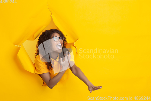 Image of Cheerful young woman poses in torn yellow paper hole background, emotional and expressive