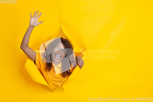 Image of Cheerful young woman poses in torn yellow paper hole background, emotional and expressive