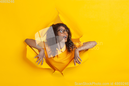 Image of Cheerful young woman poses in torn yellow paper hole background, emotional and expressive