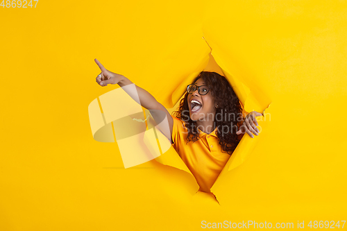 Image of Cheerful young woman poses in torn yellow paper hole background, emotional and expressive