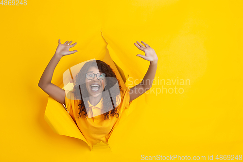 Image of Cheerful young woman poses in torn yellow paper hole background, emotional and expressive