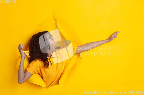 Image of Cheerful young woman poses in torn yellow paper hole background, emotional and expressive