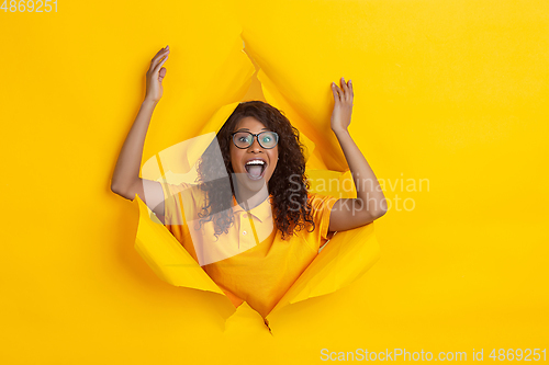 Image of Cheerful young woman poses in torn yellow paper hole background, emotional and expressive