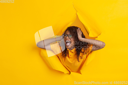 Image of Cheerful young woman poses in torn yellow paper hole background, emotional and expressive