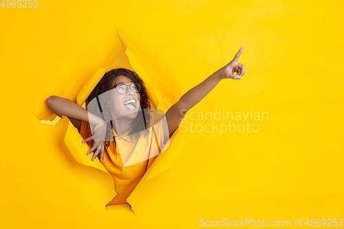 Image of Cheerful young woman poses in torn yellow paper hole background, emotional and expressive