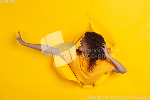 Image of Cheerful young woman poses in torn yellow paper hole background, emotional and expressive