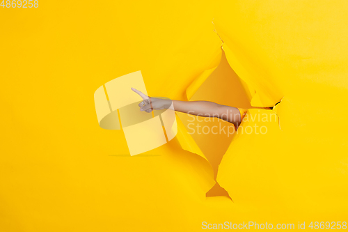 Image of Female hand pointing in torn yellow paper hole background, celebration