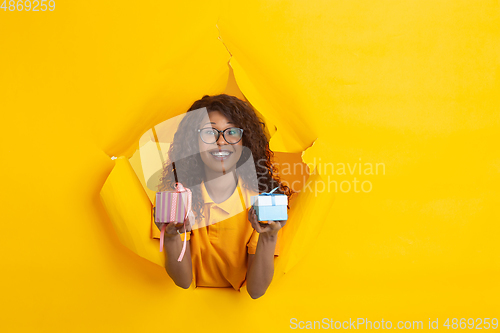 Image of Cheerful young woman poses in torn yellow paper hole background, emotional and expressive