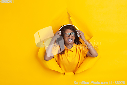 Image of Cheerful young woman poses in torn yellow paper hole background, emotional and expressive