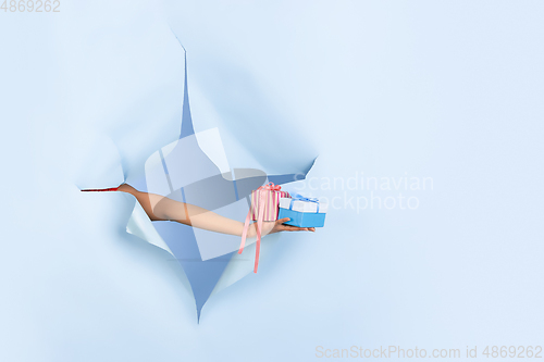 Image of Female hand giving gift in torn blue paper hole background, celebration