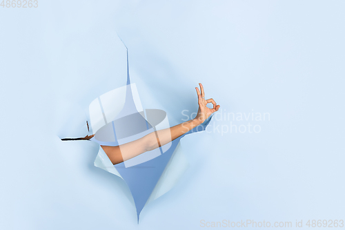 Image of Female hand pointing in torn blue paper hole background, celebration