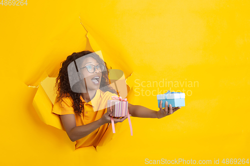 Image of Cheerful young woman poses in torn yellow paper hole background, emotional and expressive