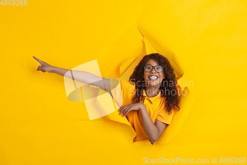 Image of Cheerful young woman poses in torn yellow paper hole background, emotional and expressive
