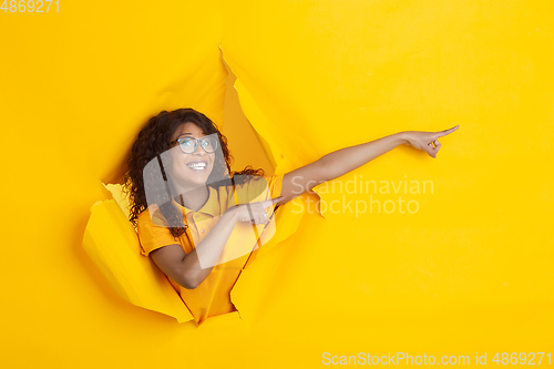 Image of Cheerful young woman poses in torn yellow paper hole background, emotional and expressive