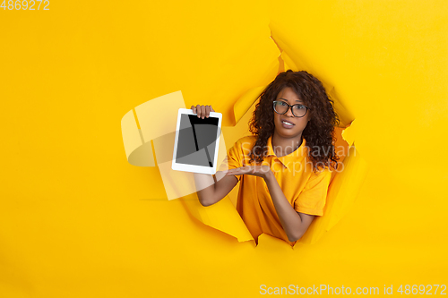 Image of Cheerful young woman poses in torn yellow paper hole background, emotional and expressive