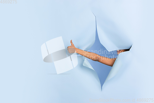 Image of Female hand pointing in torn blue paper hole background, celebration