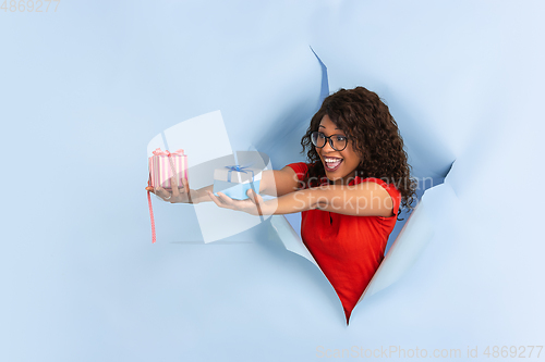 Image of Cheerful young woman poses in torn blue paper hole background, emotional and expressive