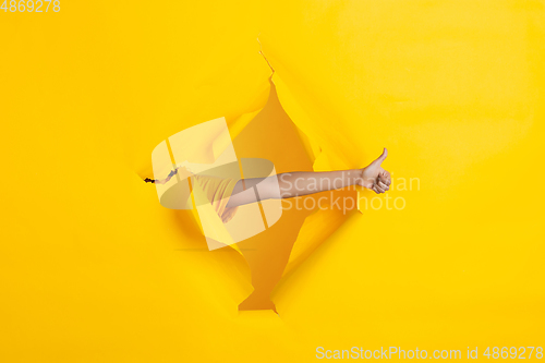 Image of Female hand pointing in torn yellow paper hole background, celebration