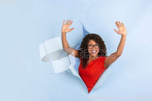 Image of Cheerful young woman poses in torn blue paper hole background, emotional and expressive