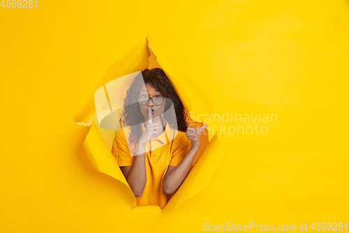 Image of Cheerful young woman poses in torn yellow paper hole background, emotional and expressive