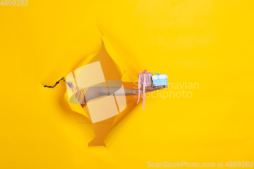 Image of Female hand giving gift in torn yellow paper hole background, celebration