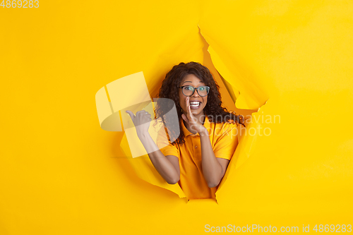 Image of Cheerful young woman poses in torn yellow paper hole background, emotional and expressive