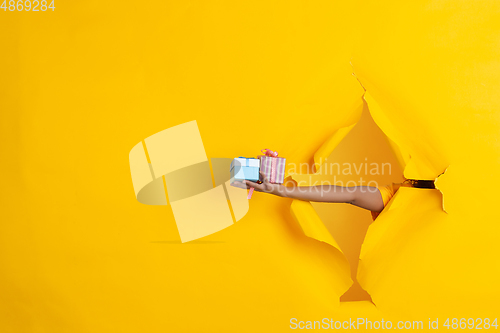 Image of Female hand giving gift in torn yellow paper hole background, celebration