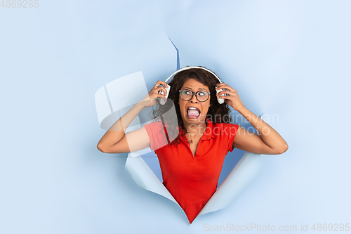 Image of Cheerful young woman poses in torn blue paper hole background, emotional and expressive