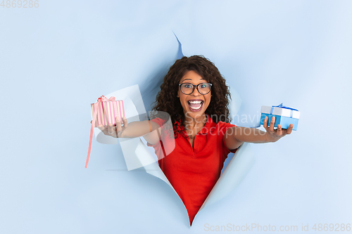 Image of Cheerful young woman poses in torn blue paper hole background, emotional and expressive