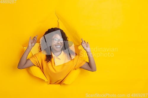 Image of Cheerful young woman poses in torn yellow paper hole background, emotional and expressive