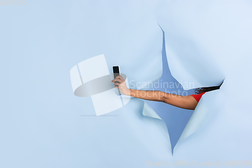 Image of Female hand giving smartphone in torn blue paper hole background, celebration
