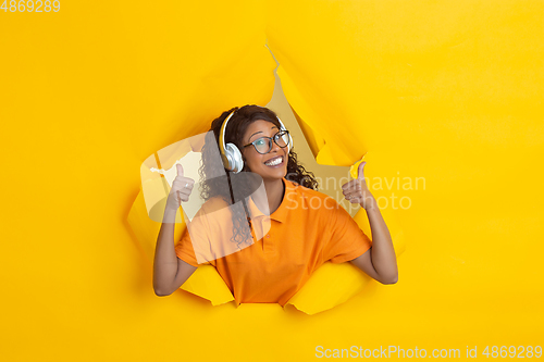 Image of Cheerful young woman poses in torn yellow paper hole background, emotional and expressive