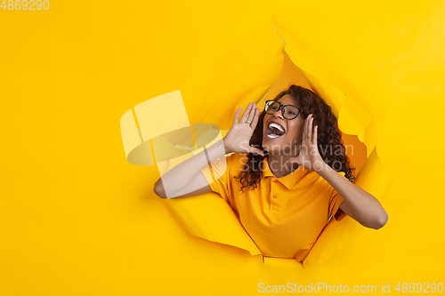 Image of Cheerful young woman poses in torn yellow paper hole background, emotional and expressive