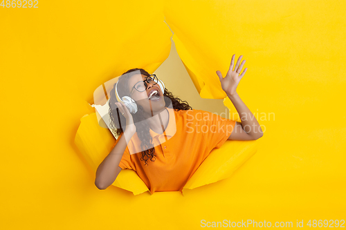 Image of Cheerful young woman poses in torn yellow paper hole background, emotional and expressive