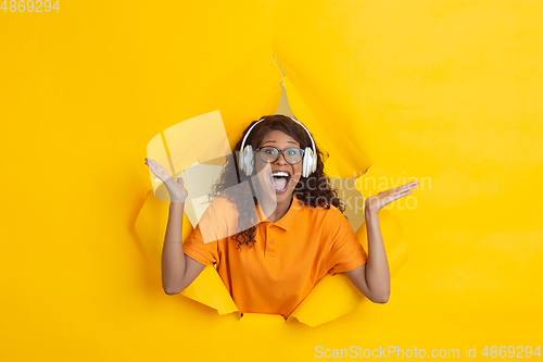 Image of Cheerful young woman poses in torn yellow paper hole background, emotional and expressive