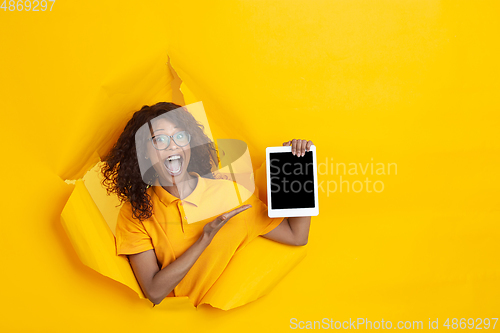 Image of Cheerful young woman poses in torn yellow paper hole background, emotional and expressive