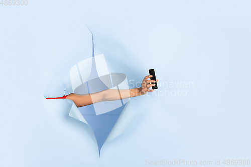 Image of Female hand giving smartphone in torn blue paper hole background, celebration