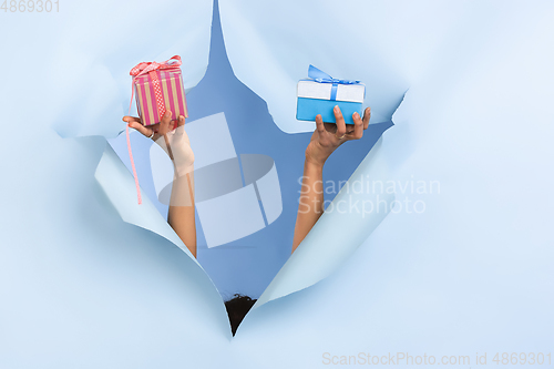 Image of Female hand giving gift in torn blue paper hole background, celebration