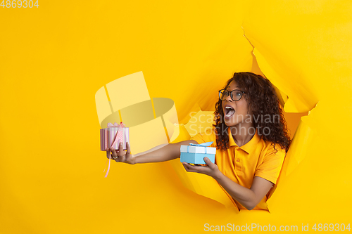 Image of Cheerful young woman poses in torn yellow paper hole background, emotional and expressive