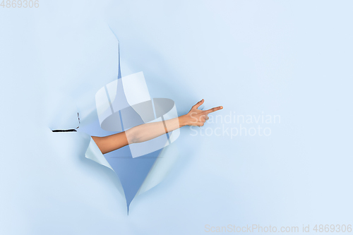 Image of Female hand pointing in torn blue paper hole background, celebration