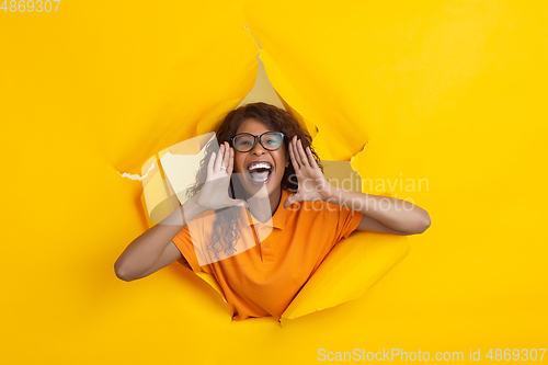 Image of Cheerful young woman poses in torn yellow paper hole background, emotional and expressive