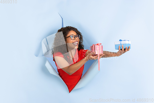 Image of Cheerful young woman poses in torn blue paper hole background, emotional and expressive