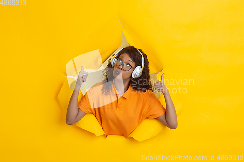 Image of Cheerful young woman poses in torn yellow paper hole background, emotional and expressive