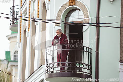 Image of Mature senior older man during quarantine, realizing how important stay at home during virus outbreak, drinking coffee on the balcony