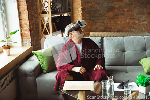 Image of Mature senior older man during quarantine, realizing how important stay at home during virus outbreak, trying on VR-headset, playing, watching