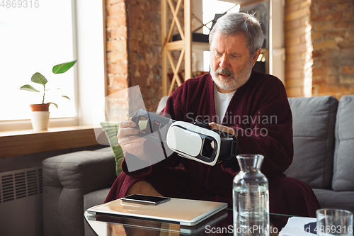 Image of Mature senior older man during quarantine, realizing how important stay at home during virus outbreak, trying on VR-headset, playing, watching