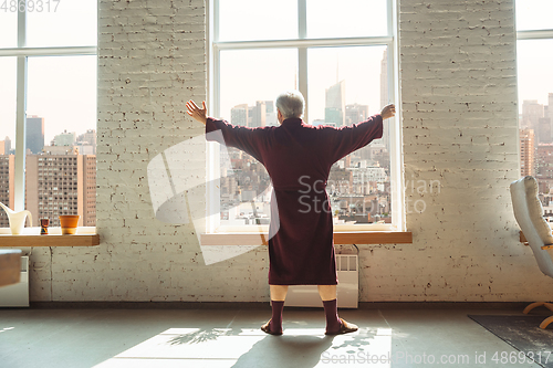 Image of Mature senior older man during quarantine, realizing how important stay at home during virus outbreak, looking throught window on day city New York