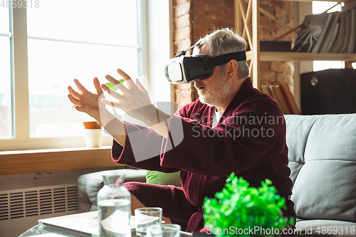 Image of Mature senior older man during quarantine, realizing how important stay at home during virus outbreak, trying on VR-headset, playing, watching