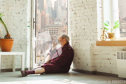 Image of Mature senior older man during quarantine, realizing how important stay at home during virus outbreak, looking throught window on day New York city